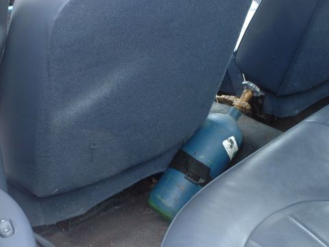 1999 Ford Crown Victoria - A blue tank with a brass valve is secured between the seats of a vehicle.