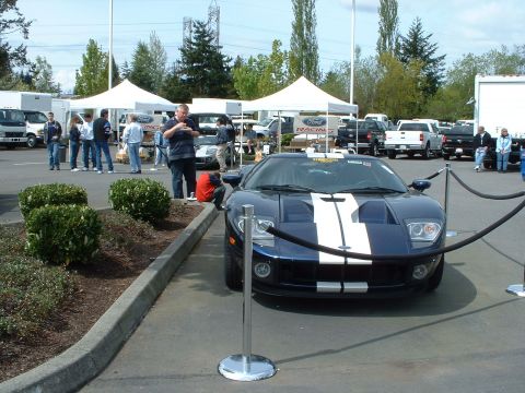 1999 Ford Crown Victoria - A dark blue Ford GT with white racing stripes is displayed at an outdoor event with tents and other vehicles in the background.
