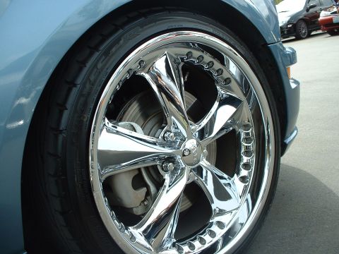 1999 Ford Crown Victoria - Close-up of a custom chrome wheel on a blue vehicle, with other cars parked nearby.