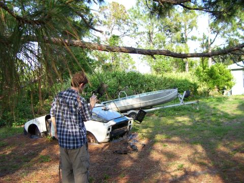 1994 Ford Probe - A person stands near a damaged car body and a boat on a trailer in a grassy, wooded area.