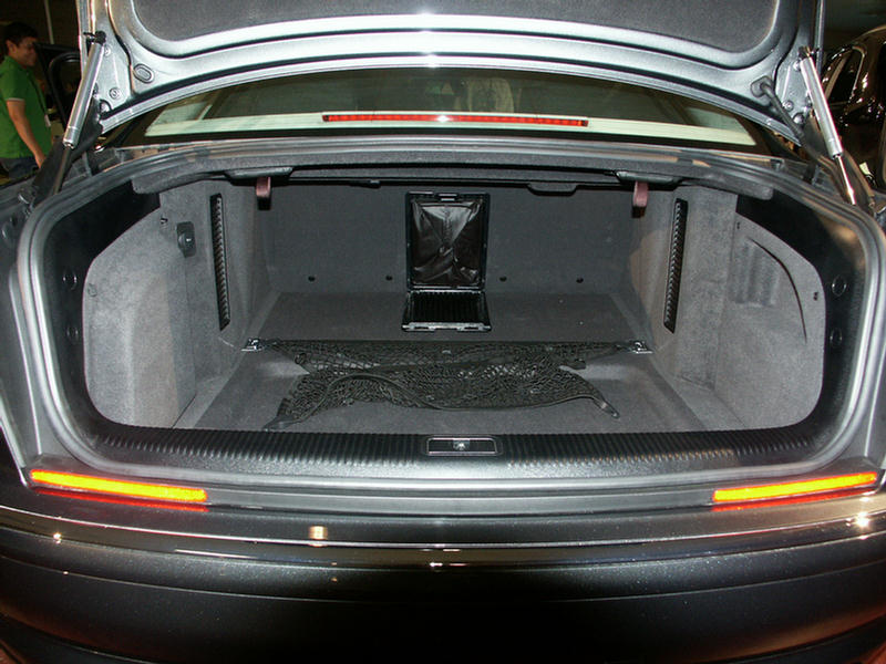 Car trunk with cargo net and a black bag. A person in a green shirt is visible in the background