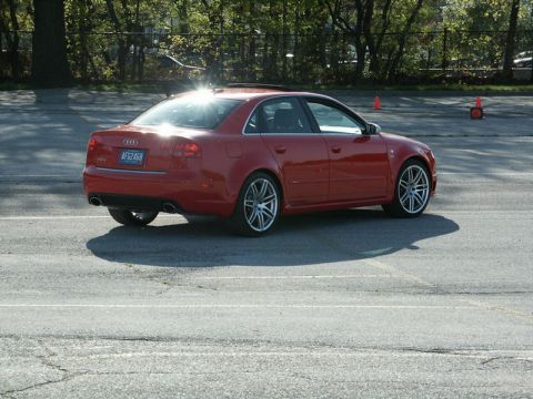 2001 Mercury Grand Marquis - A red Audi sedan is captured in a rear 3/4 view on a paved surface, with trees and orange cones in the background.