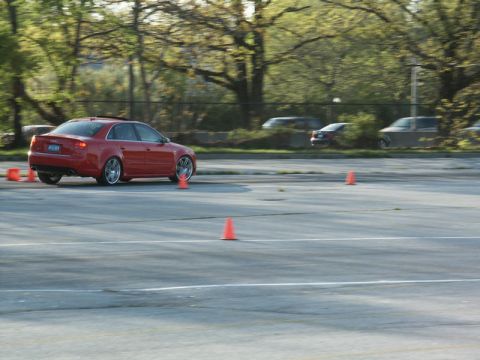 2001 Mercury Grand Marquis - A red sedan drives through a cone course on a paved lot with trees in the background.