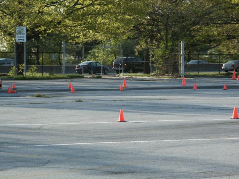 2001 Mercury Grand Marquis - A dark sedan and a black SUV are parked on a lot marked with orange traffic cones, with trees and a fence in the background.