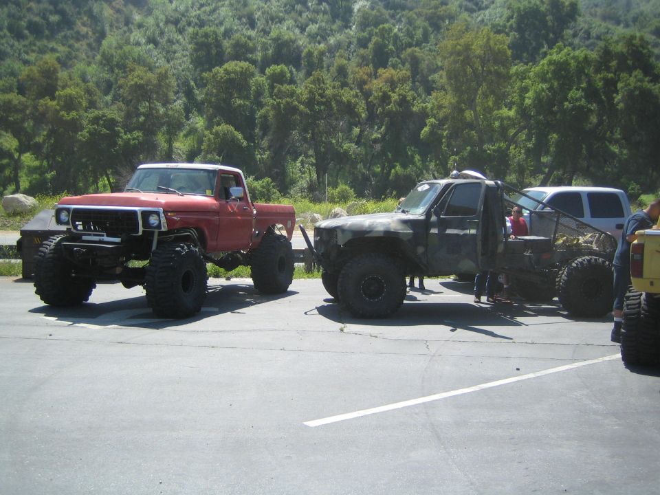 Red pickup truck with large tires and white roof, parked next to a camouflage truck