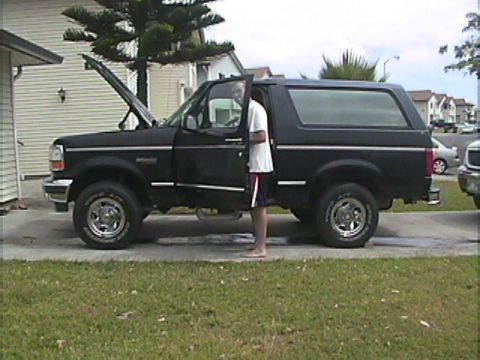 1994 Ford Bronco - A black 1994 Ford Bronco is parked with its hood open and driver's door ajar, showing a person standing in the doorway.
