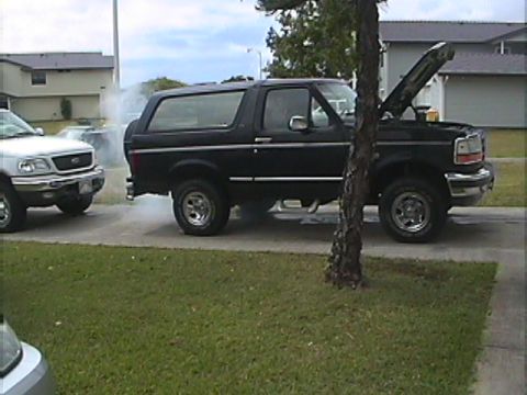 1994 Ford Bronco - A black 1994 Ford Bronco is seen with its hood open and smoke billowing from the engine compartment.