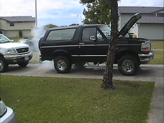 black 1994 Ford Bronco with hood up, smoke from engine, parked next to a silver Ford F-150