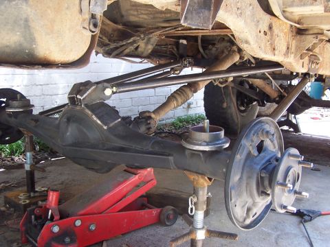 1987 Ford Bronco - Custom suspension work is underway on the rear axle, adjustable control arms and support from a red hydraulic jack.