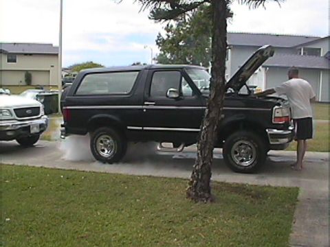 1994 Ford Bronco - Man checks engine of black 1994 Ford Bronco, with a white truck in the background.