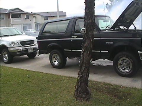 1994 Ford Bronco - A black SUV, possibly a Ford Bronco, has its hood open while parked next to a silver pickup truck.