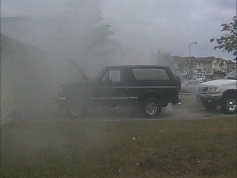 1994 Ford Bronco - A black Ford Bronco appears to be having mechanical issues, emitting smoke with its hood up.