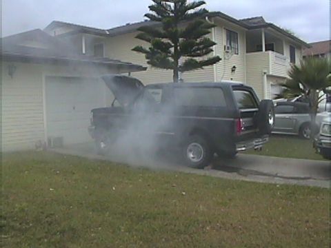 1994 Ford Bronco - A black 1994 Ford Bronco is seen emitting smoke from its open hood while parked in a residential driveway.