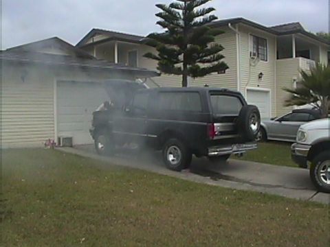 1994 Ford Bronco - A black 1994 Ford Bronco appears to be having mechanical issues, with smoke emanating from the open hood.