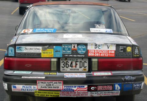 1988 Ford E250 - This car is heavily decorated with numerous bumper stickers, displaying a variety of messages and affiliations.