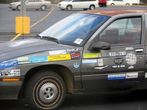 1988 Ford E250 - A dark sedan is heavily adorned with numerous stickers, including one that reads 'Corsica'.