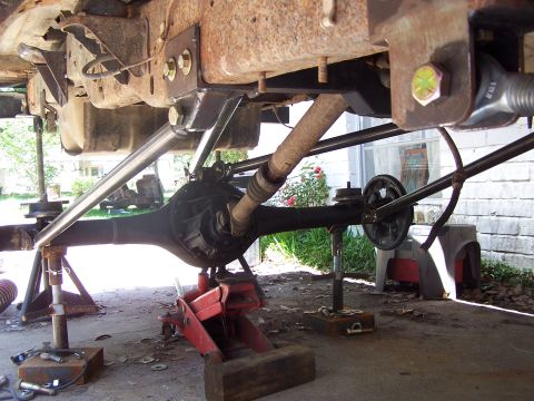 1987 Ford Bronco - Custom suspension work on a vehicle's rear axle, supported by jack stands.