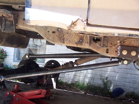 1987 Ford Bronco - Close-up view of a vehicle's undercarriage, showing modified suspension components and a rusty frame.