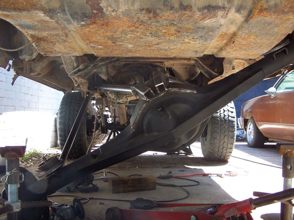 Undercarriage of a lifted vehicle showing a large rear differential and suspension modifications. Another vehicle is partially visible