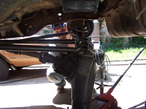 1987 Ford Bronco - Mechanic works on the suspension and differential of a vehicle, with another vehicle in the background.