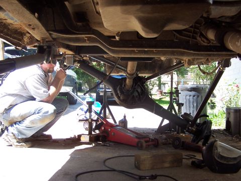 1987 Ford Bronco - A mechanic works on the rear axle assembly of a vehicle, which is raised on jack stands.