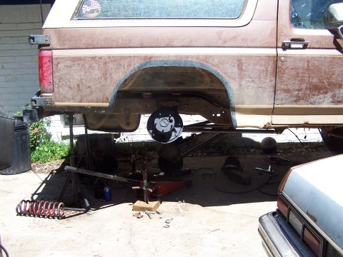 1987 Ford Bronco - A brown SUV is shown from the side with its rear wheel removed, indicating it is undergoing maintenance or repair work.