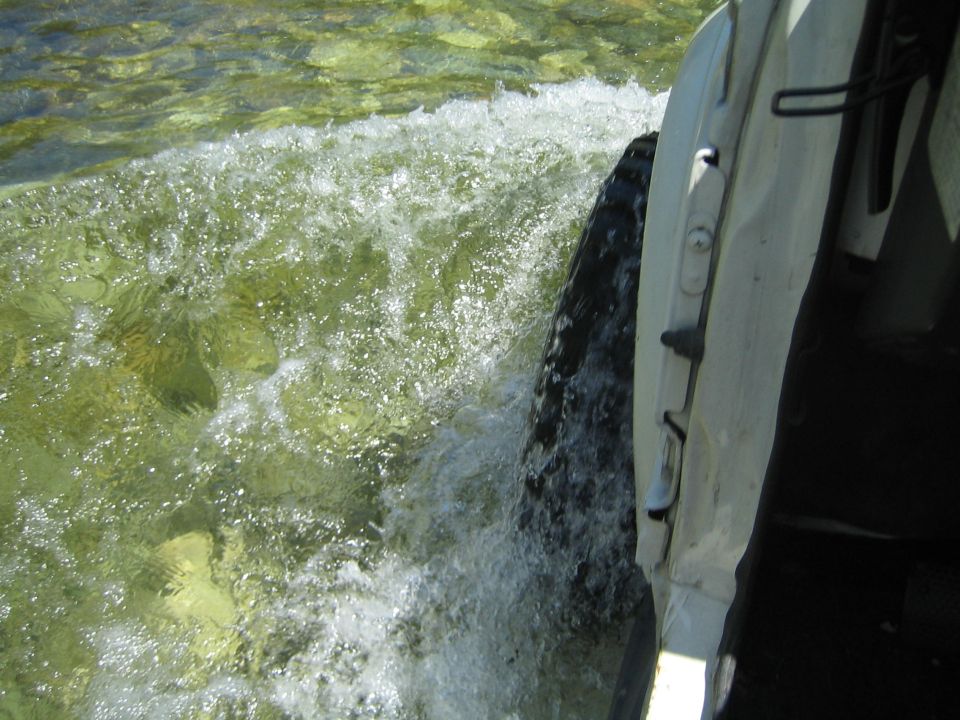 White vehicle side panel and tire splashing through clear, rocky water