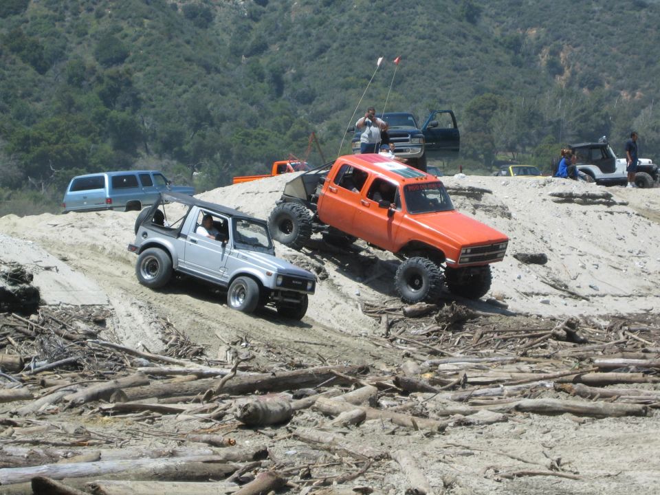 Silver Suzuki Samurai with a roll cage on a sandy incline, front 3/4 view