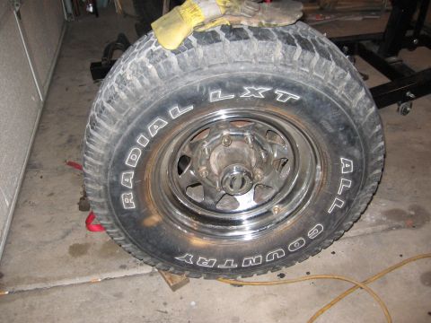 1990 Ford Bronco - A close-up view of a Radial LXT Country All-Terrain tire mounted on a chrome wheel, with a pair of work gloves resting on top.