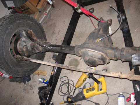 1990 Ford Bronco - Front axle assembly with tire and brake components, resting on a stand.