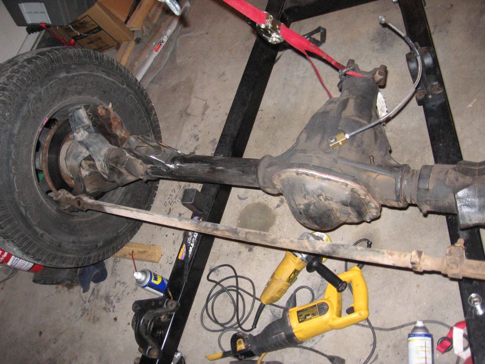 Front axle assembly with tire, brake rotor, and tie rod. Tools like a reciprocating saw and angle grinder are nearby
