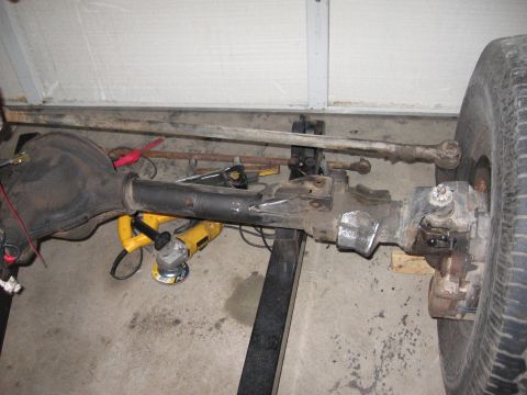 1990 Ford Bronco - Front axle assembly with disc brake and tie rod, supported by jack stands in a garage setting.