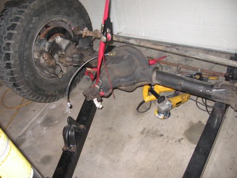 1990 Ford Bronco - Front axle assembly, likely from a Ford Bronco, with a tire and angle grinder nearby.