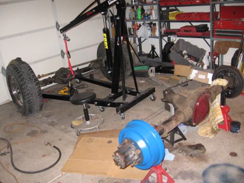 1990 Ford Bronco - Garage scene with vehicle axles and an engine hoist, suggesting repair or modification work.