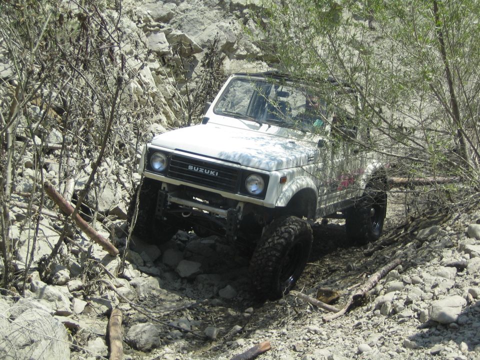 White 1987 Suzuki Samurai navigating a rocky, overgrown trail