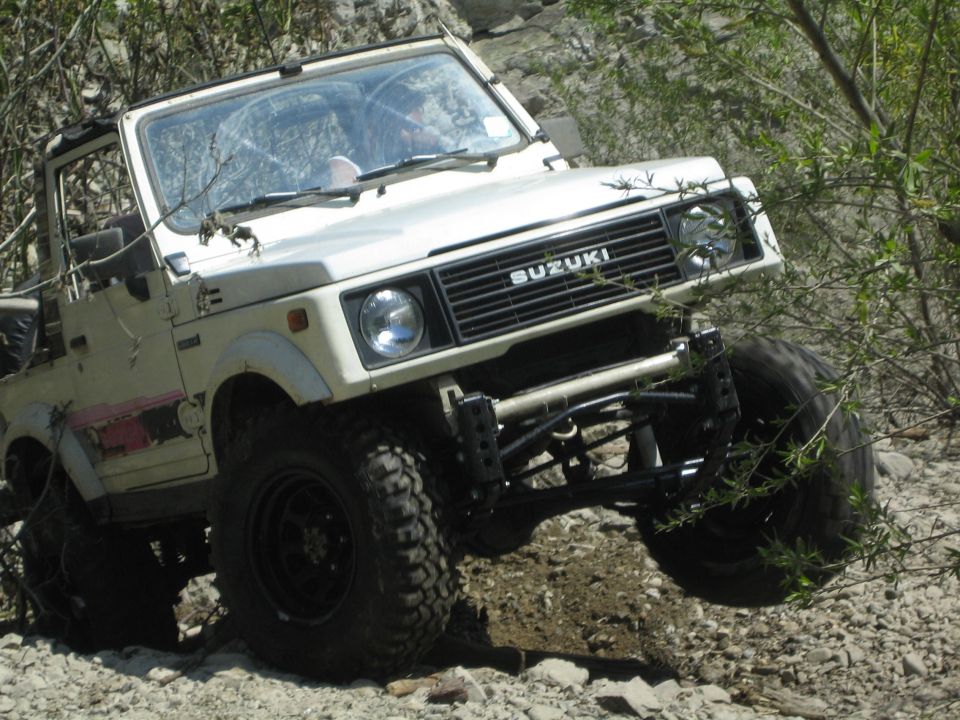 White 1987 Suzuki Samurai with off-road tires navigating rocky terrain