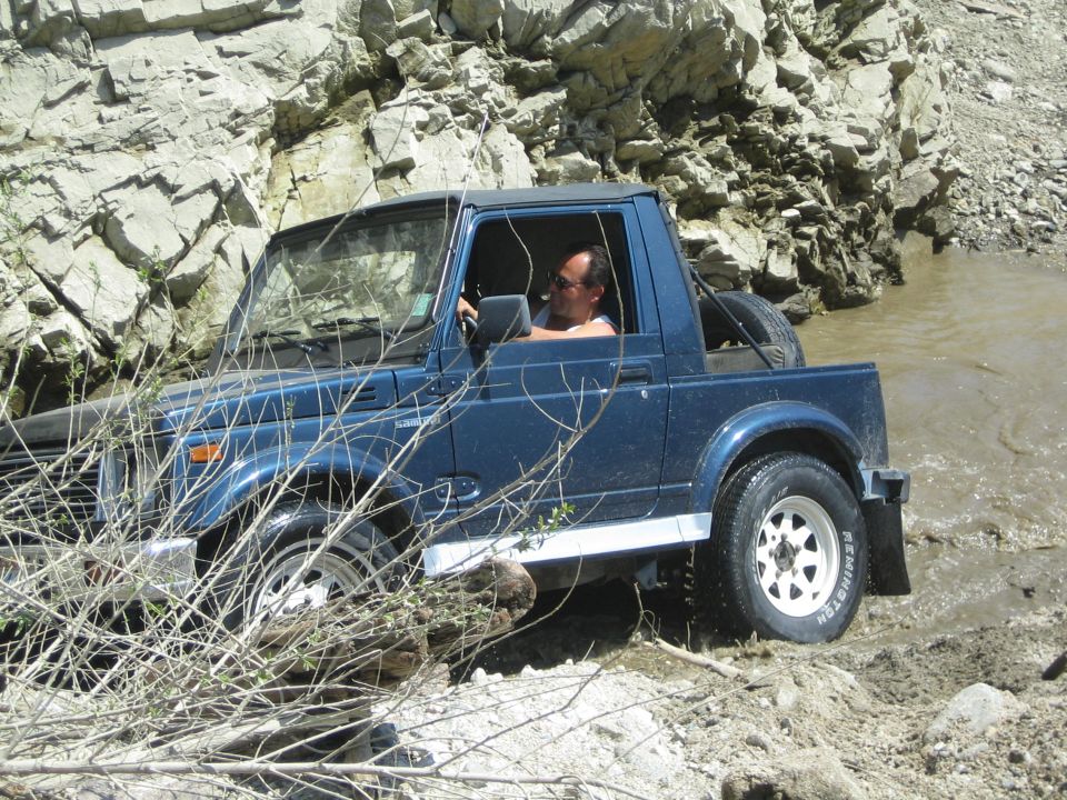 Blue Suzuki Samurai navigating a rocky stream, driver visible