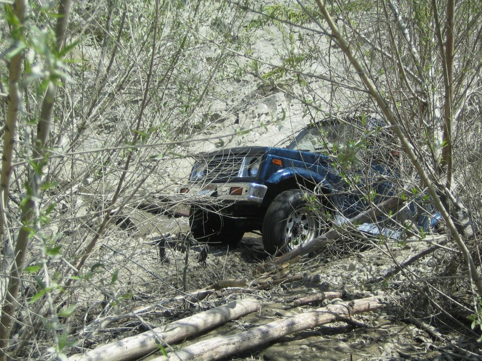 Blue Suzuki Samurai off-roading through brush and logs