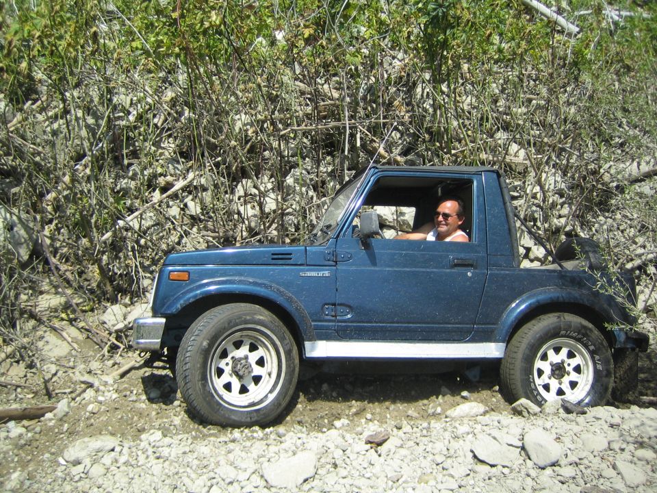 Blue 1987 Suzuki Samurai parked on rocky terrain with a man driving