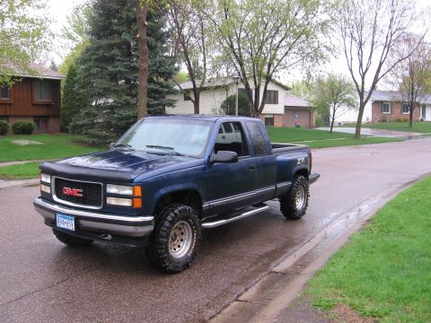 1995 GMC Sierra 1500 - This GMC pickup truck is parked on a wet residential street with houses and trees in the background.