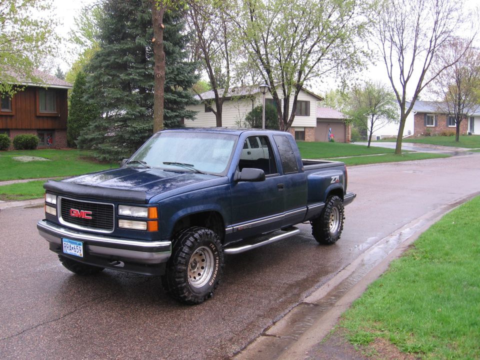 Blue GMC pickup truck parked on a wet residential street