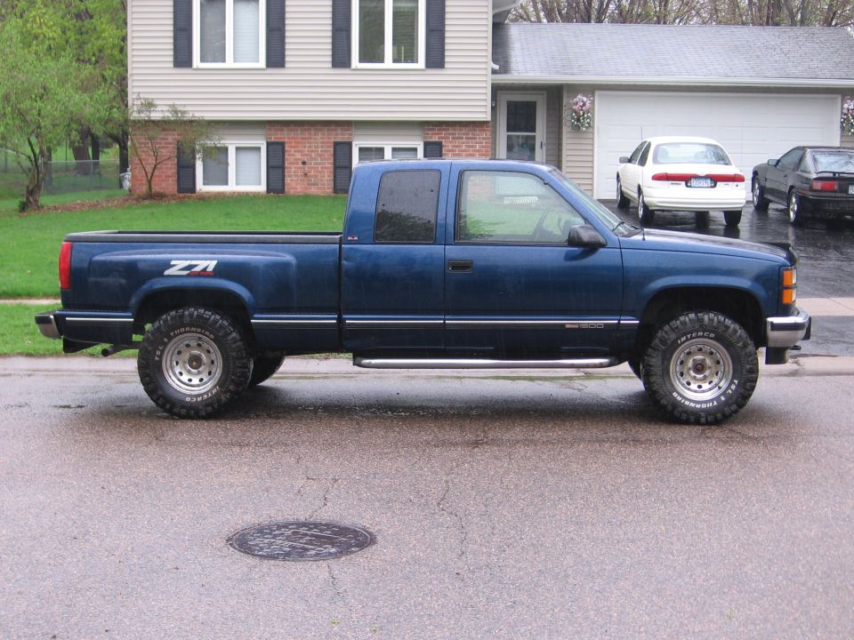 Blue 1995 GMC Sierra 1500 pickup truck parked on a wet street in front of a house