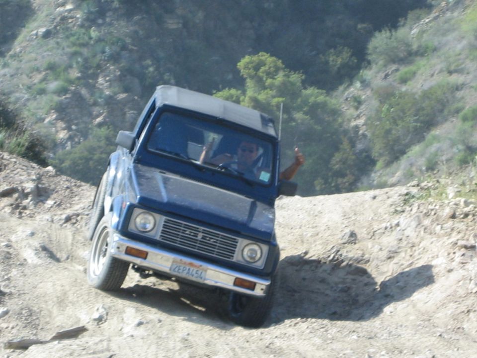 Blue 1987 Suzuki Samurai driving off-road with driver giving a thumbs up