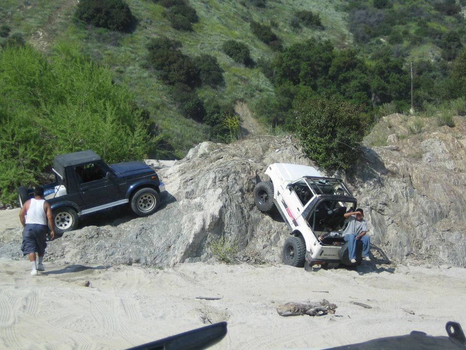 White off-road vehicle tilted on rocks, dark vehicle on incline