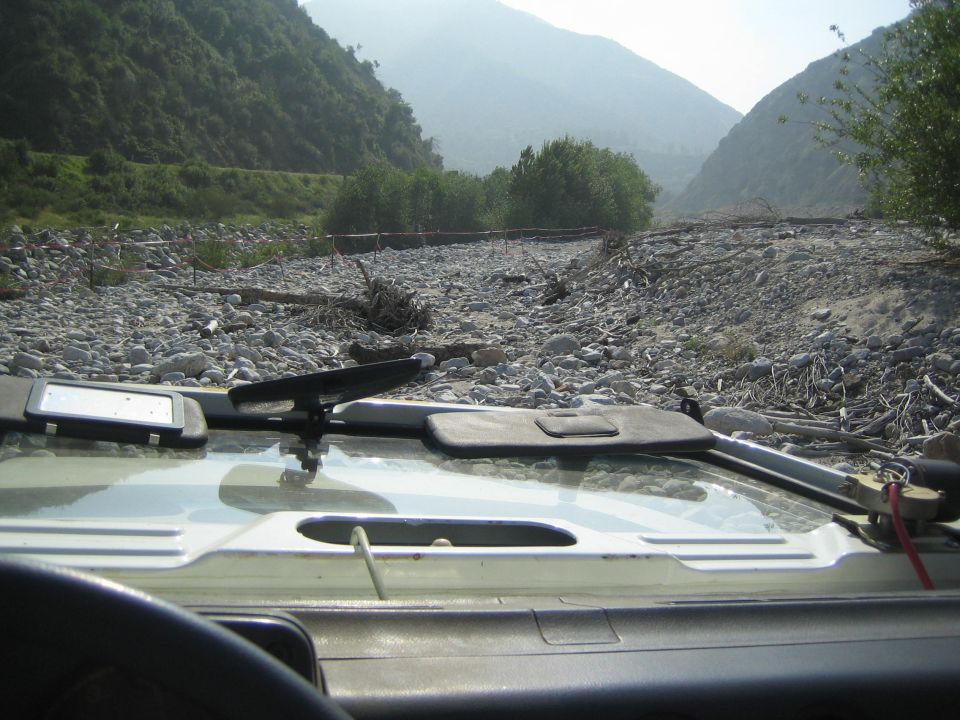 View from inside a vehicle driving through a rocky riverbed in a canyon