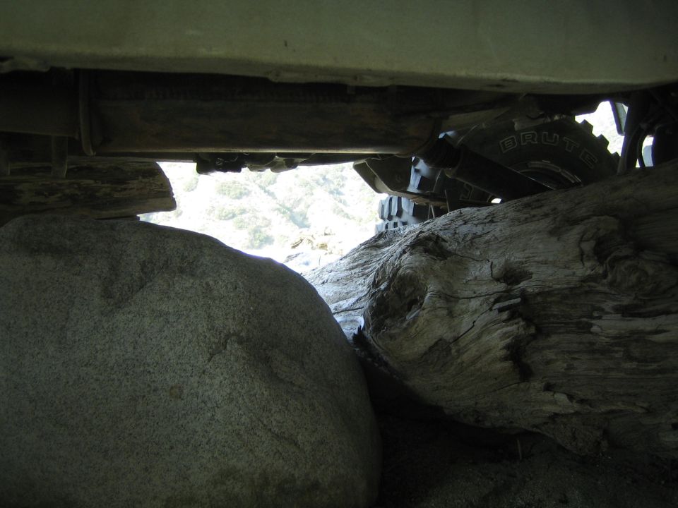 Underside view of a vehicle with large rocks and logs beneath it
