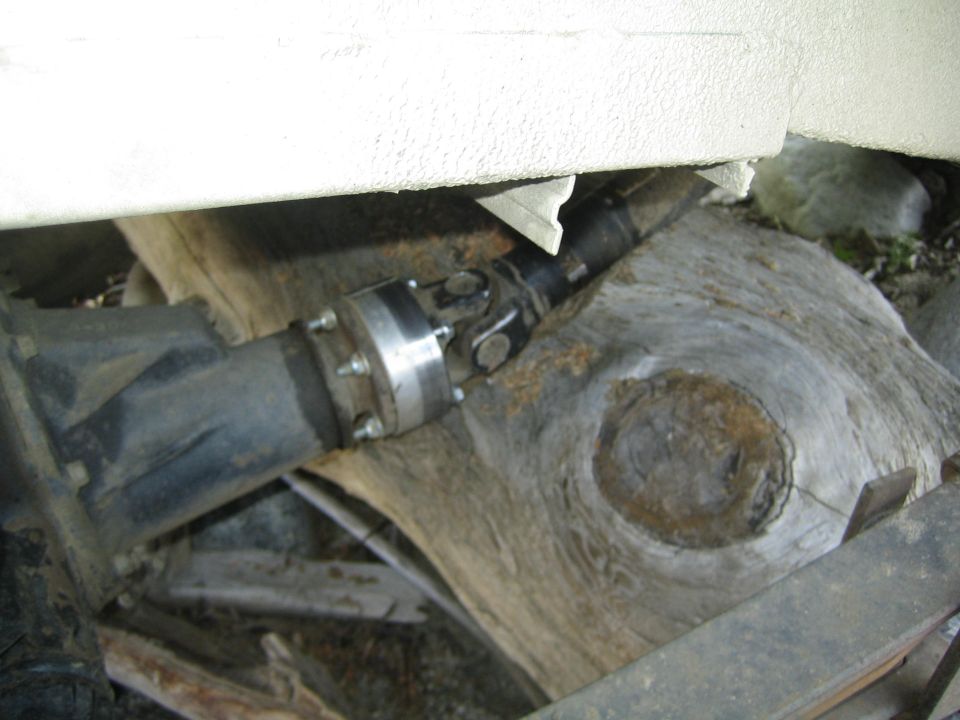 close-up of a vehicle's driveshaft and U-joint, resting on large rocks and wood