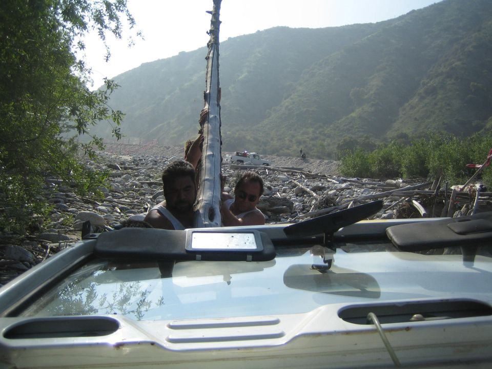 Interior view of a light-colored vehicle with two men carrying a long pole, mountains in background