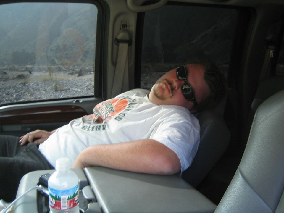 Man sleeping in passenger seat of a vehicle, wearing sunglasses and a t-shirt