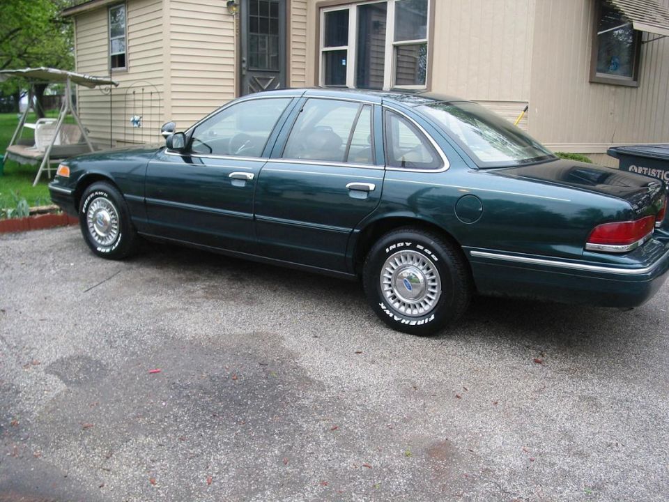 1996 Ford Crown Victoria sedan, dark green, parked on asphalt in front of a house